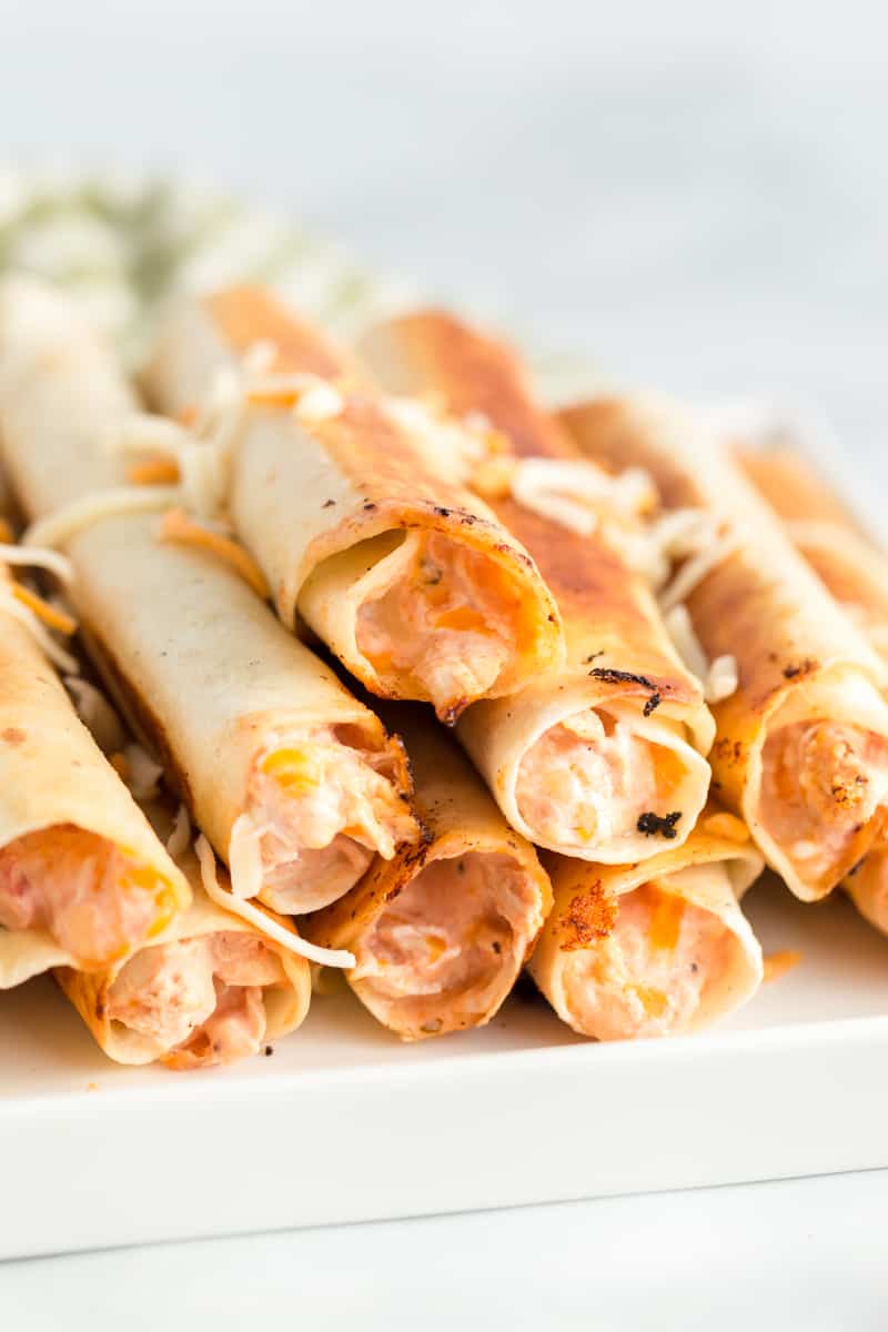 Golden Chicken Taquitos on plate with shredded cheese on top and creamy filling showing