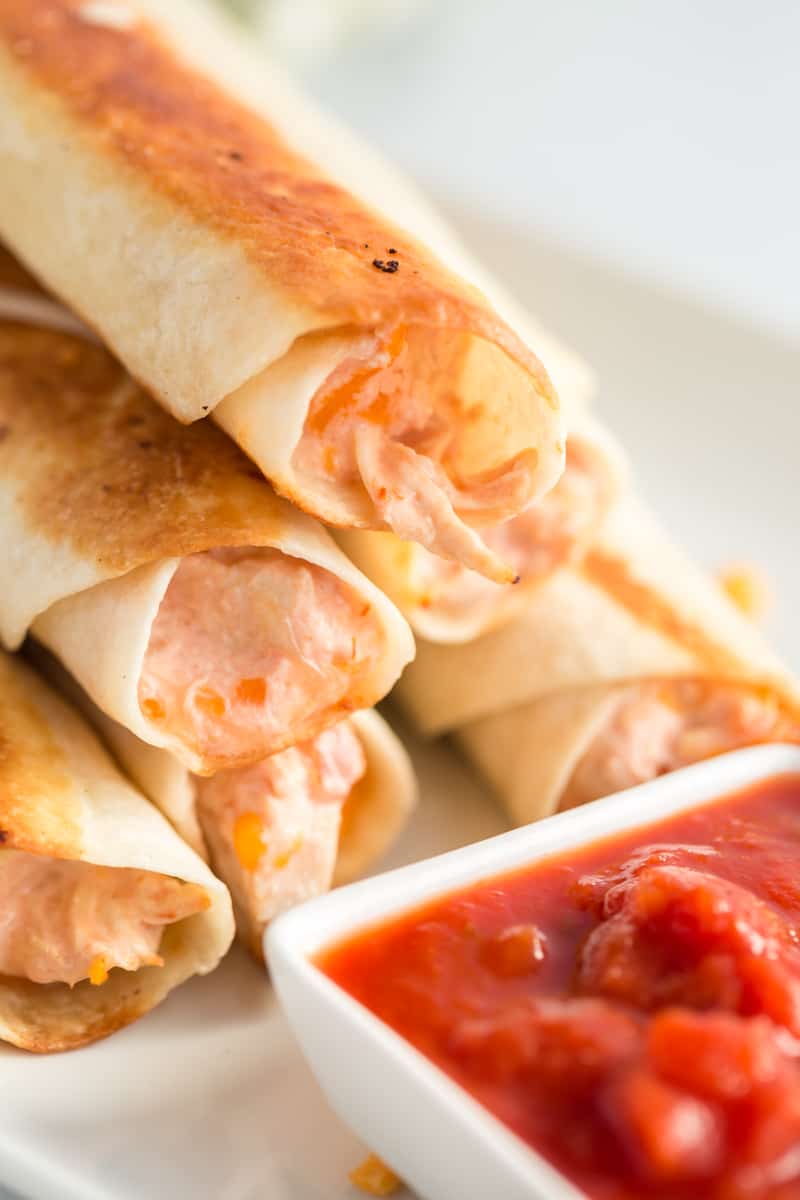 Golden chicken taquitos stacked up with salsa in dipping dish