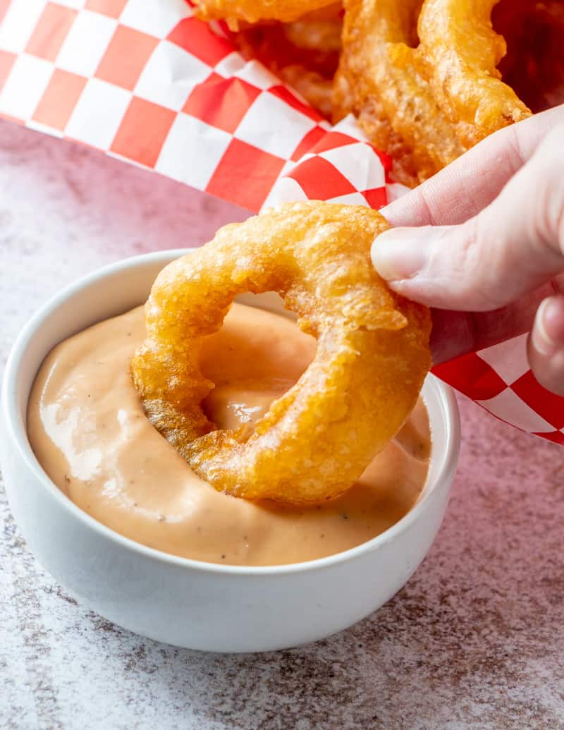 Onion ring being dipped into a dipping sauce