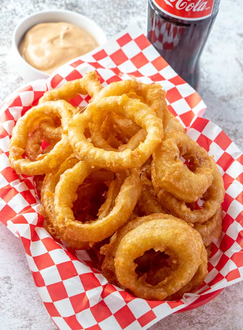 Overhead photo of beer battered onion rings in basket with coke and dipping sauce