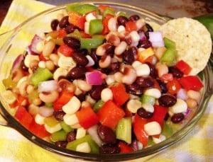 Close up photo of cowboy caviar whooping off beans, tomatoes, onions in glass dish