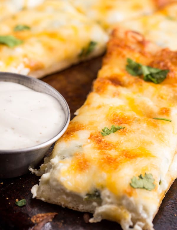 Sliced breadstick topped with cilantro next to ranch in dipping bowl