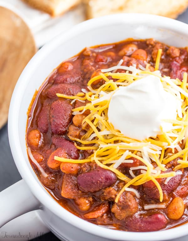 Overhead photo of chili in white handled bowl topped with shredded cheese and sour cream