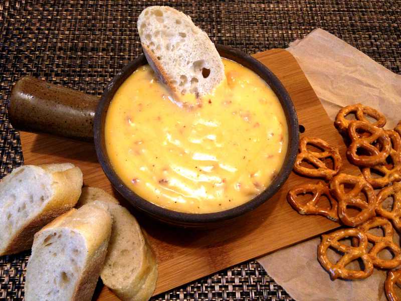Overhead photo of beer cheese dip in brown dish surrounded by bread and pretzels