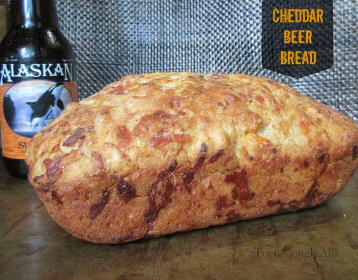 Finished loaf of cheddar beer bread on baking sheet with beer in background