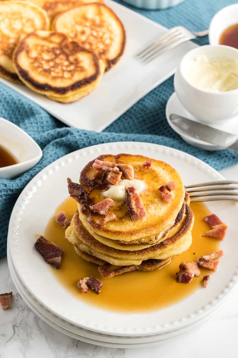 Hoe cakes with the cheddar and bacon option on plate with syrup and bacon
