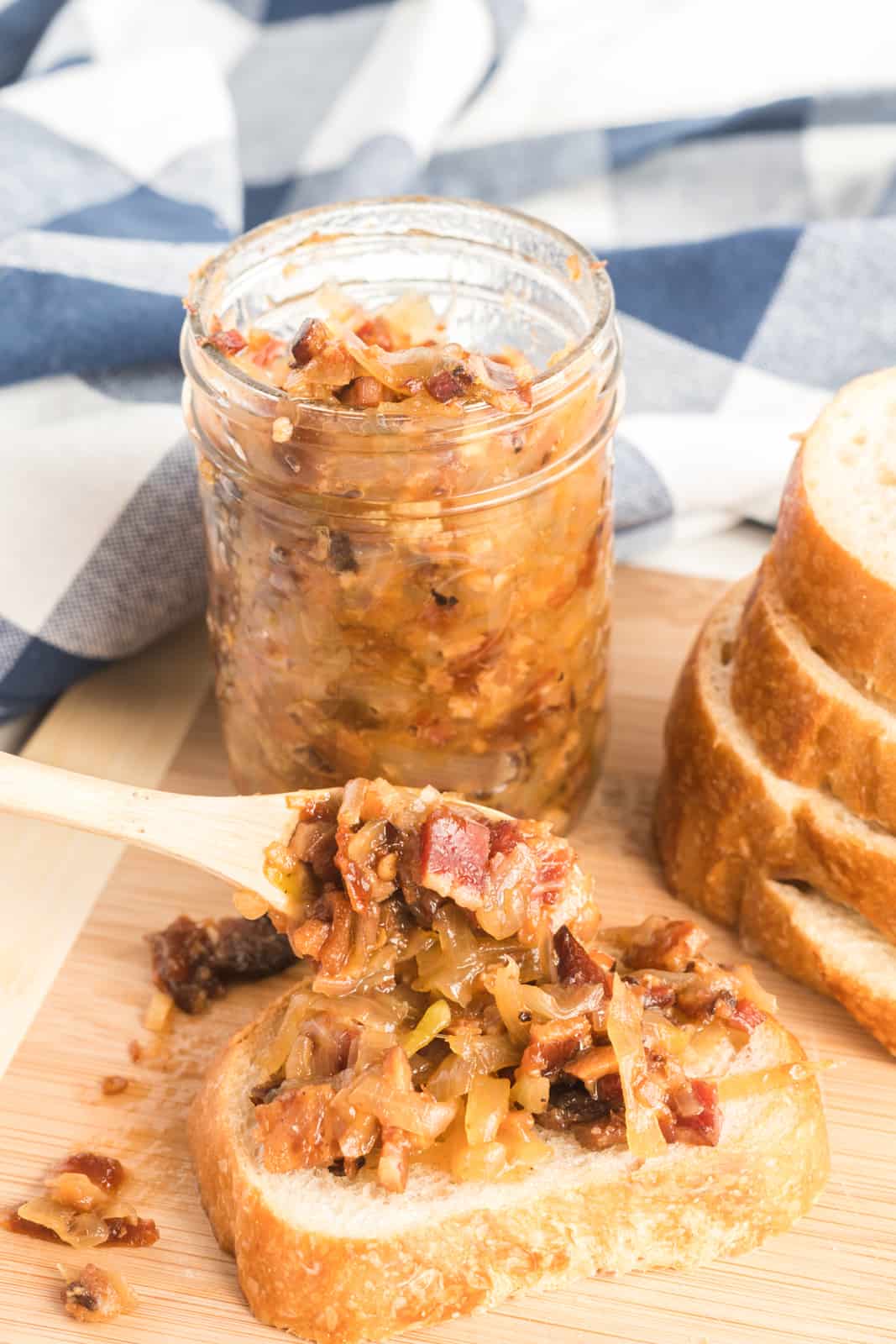 Spoon spooning some bacon jam onto slice of bread with canning jar in background