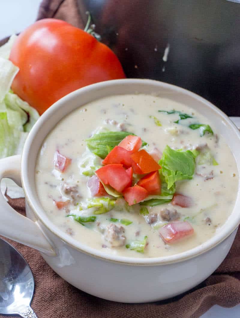 Cheeseburger Soup in white handled bowl topped with lettuce and diced tomatoes 