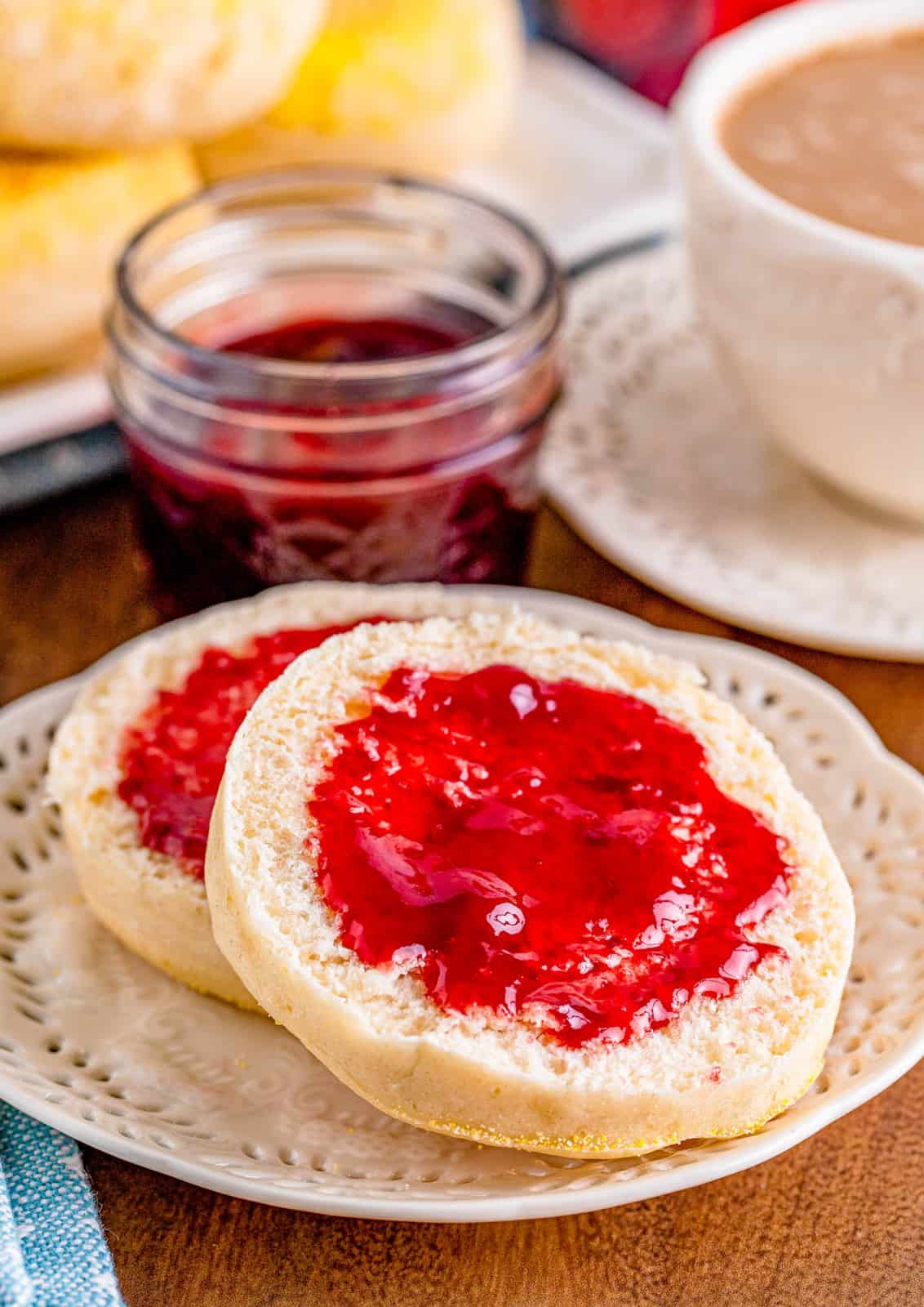 One split English Muffin on white plate spread with jelly.