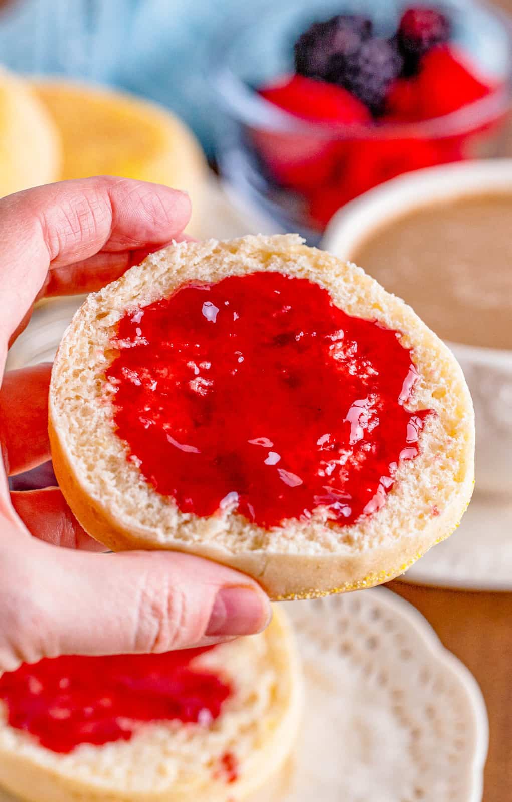 Hand holding up one side of English Muffin showing jelly.