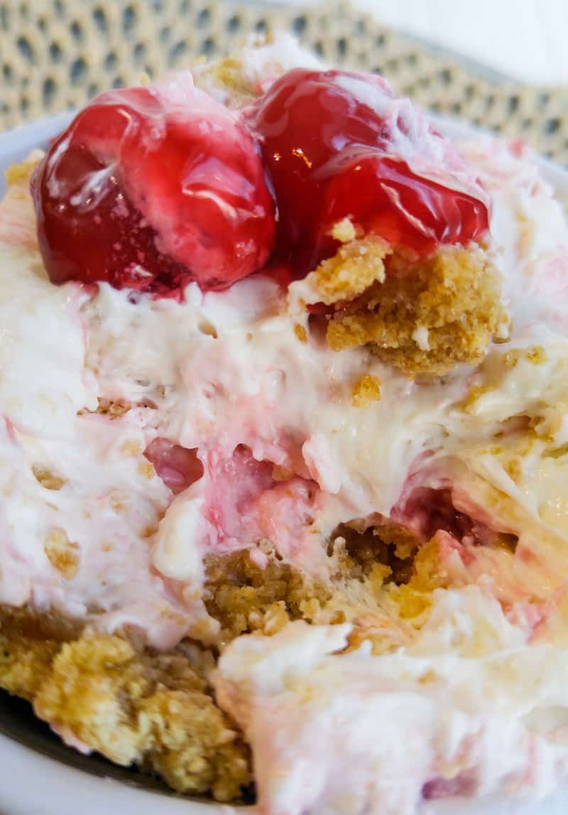Up close of cheesecake fluff in owl showing creamy filling, cherries and graham cracker crumbs