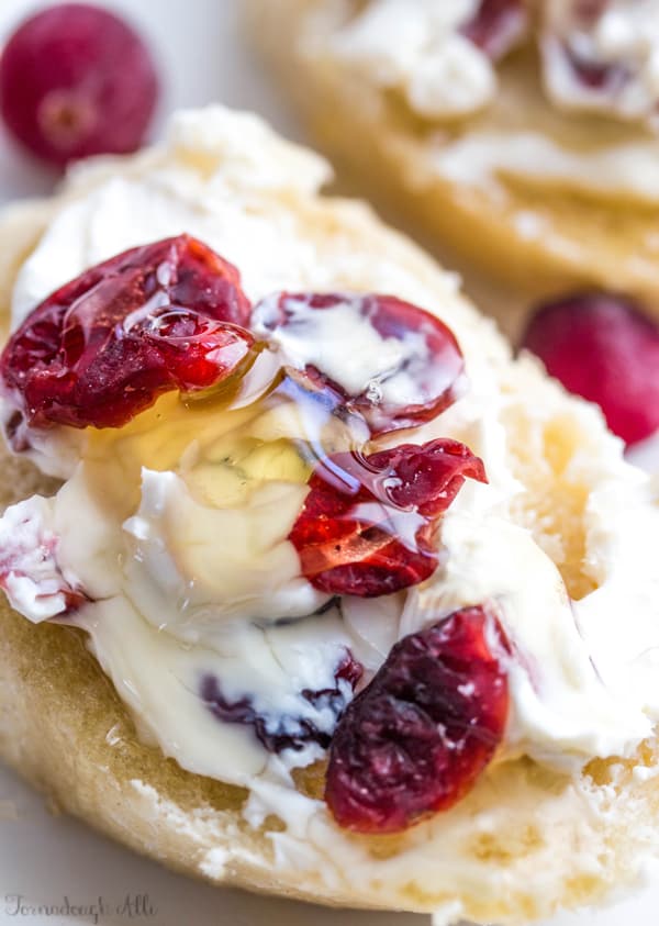 Close up of goat cheese on sliced baguette topped with dried cranberries and honey