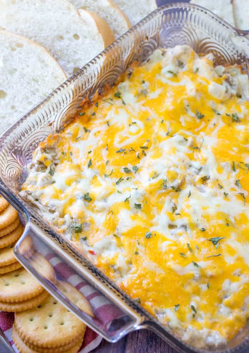 Finished cheese top mushroom dip in serving dish surrounded by sliced bread and crackers