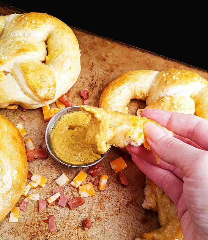 Hand dipping portion of pretzel in mustard