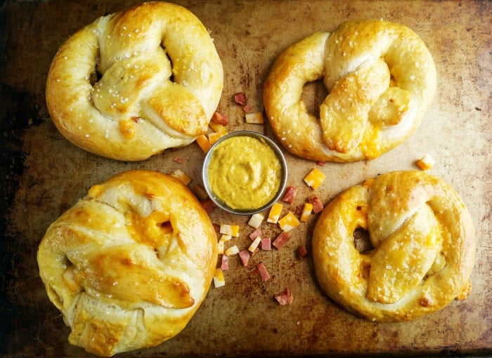 Overhead of four pretzels on baking sheet with spicy mustard in serving bowl