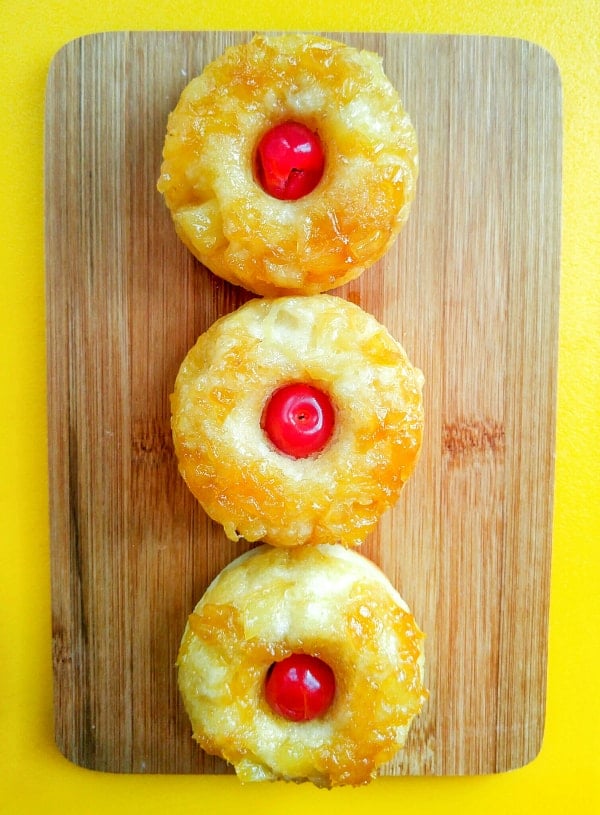 Overhead of three donuts with cherry in center on wooden board