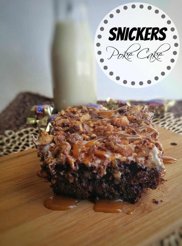 Snickers Poke Cake slice on wooden board with dripping caramel