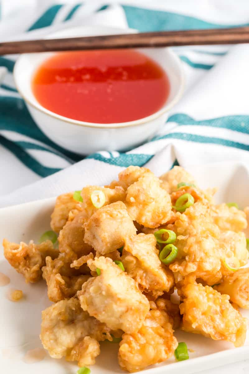 Chinese chicken on plate with green onions and sweet and sour sauce in background