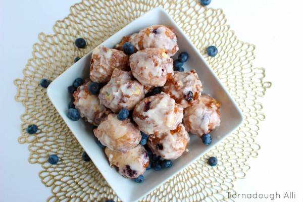 Overhead of glazed fritters in white dish garnished with blueberries