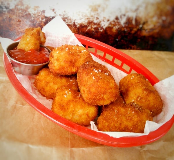 Red bar basket full of Cheesy Tater Tots with one tater tot in ketchup cup