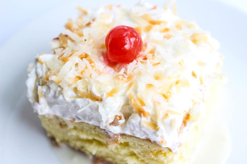 Slice of cake on plate with whipped topping, coconut and cherry