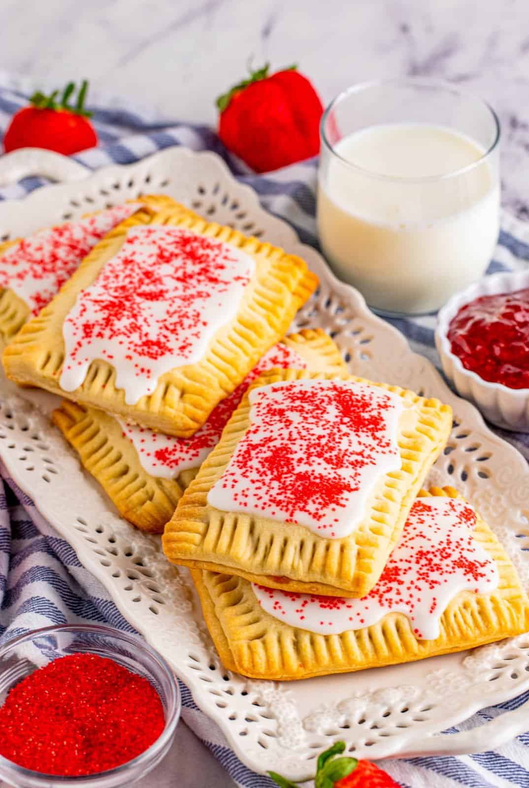 Stacked Strawberry Pop-Tarts on white platter with milk and preserves next to it.
