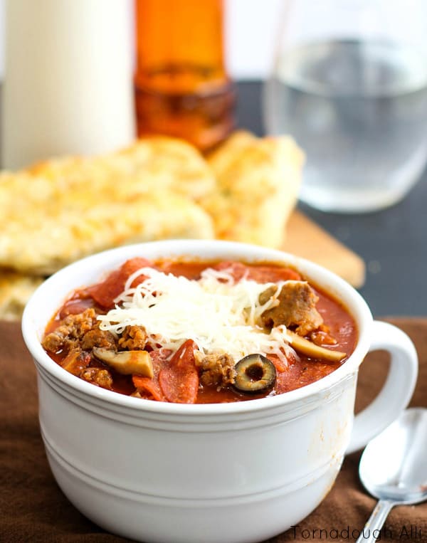 Handled white bowl holding Pizza Chili with breadsticks in background