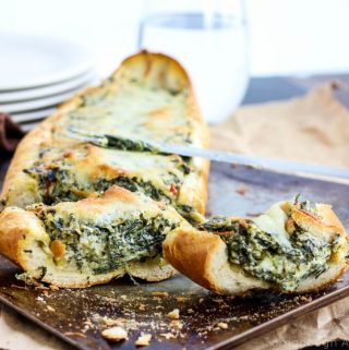 Two cut slices of Spinach Dip Stuffed French Bread in front of loaf