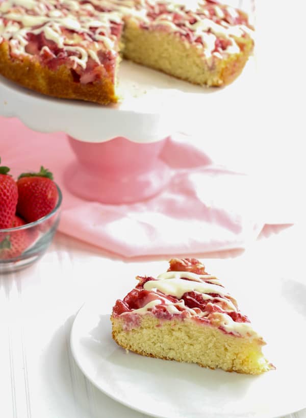 Slice of Strawberries and Cream Cake on white plate with cake on cake stand in background