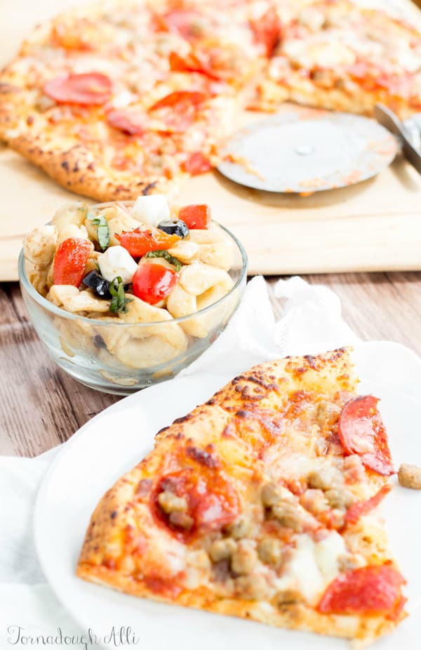 Caprese Tortellini Salad in bowl with slice of pizza in front of it