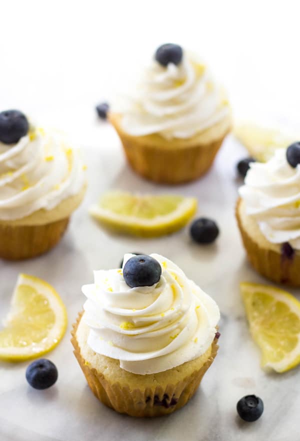 Overhead of four cupcakes on platter garnished with lemons and blueberries