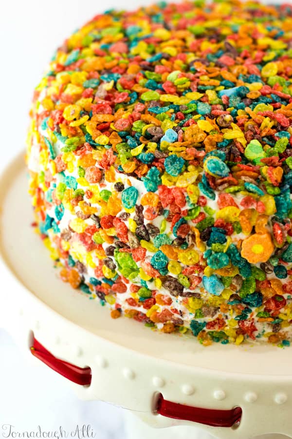 Marshmallow Fruity Pebbles Cake on cake stand covered in fruity pebbles