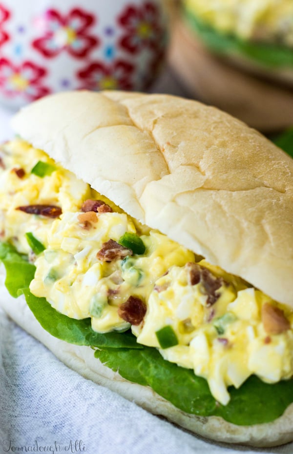 Close up of egg salad showing bits of bacon and jalapeño on bun with lettuce