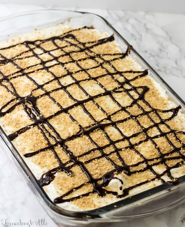 Cake in baking dish with topped with graham cracker crumbs and chocolate drizzle