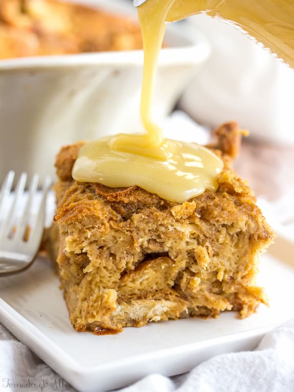 Sauce being poured over bread pudding on white plate