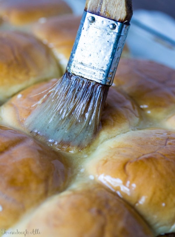 Butter being brushed on top of slider buns