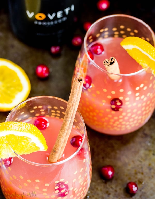 Overhead photo of Cranberry Orange Mimosas in two glasses with barges and cinnamon sticks