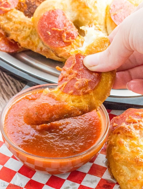 Hand dipping piece of Pepperoni Pizza Pretzel into sauce