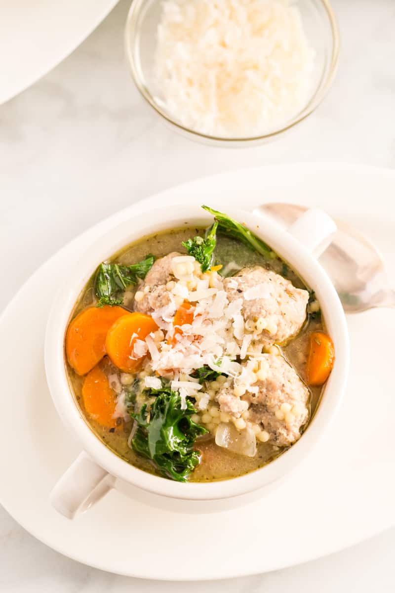 Overheat photo of italian wedding soup in bowl, with carrots, meatballs, kale and parmesan cheese