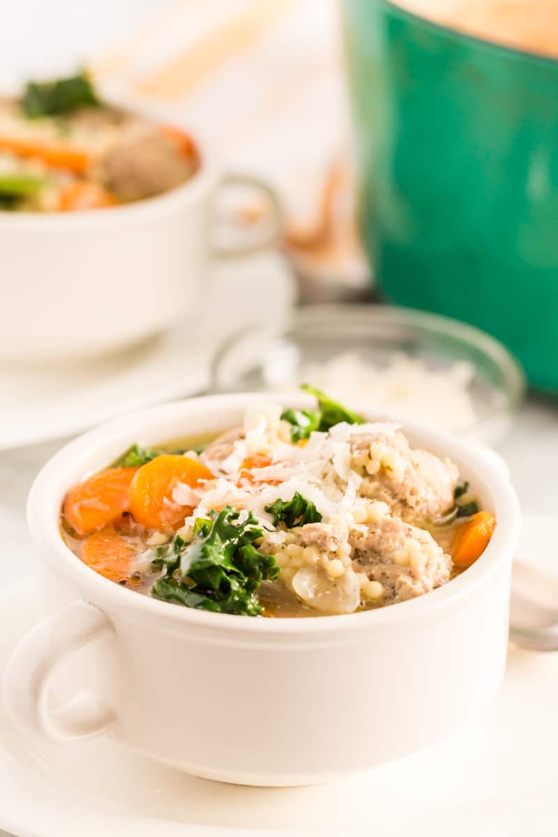Italian Wedding Soup served in white bowl topped with shredded parmesan cheese