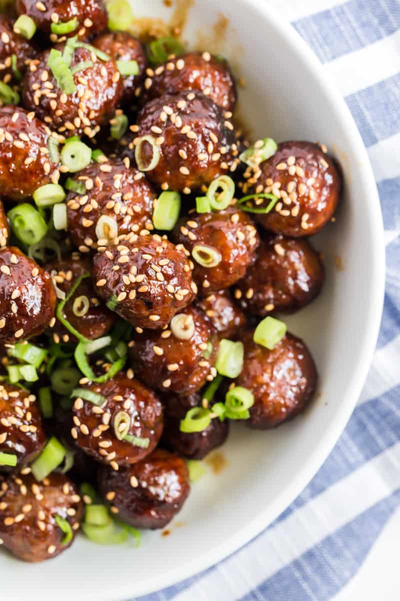 Crockpot Meatballs in bowl slathered in sauce and topped with sesame seeds and green onions