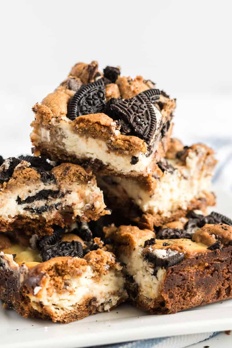 Pile of cheesecake bars on plate showing the layers of cookie dough, cheesecake and Oreos