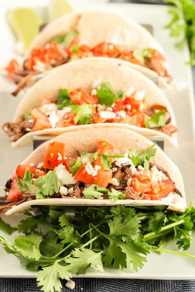 Street Tacos lined up on plate with cilantro and lime garnishes