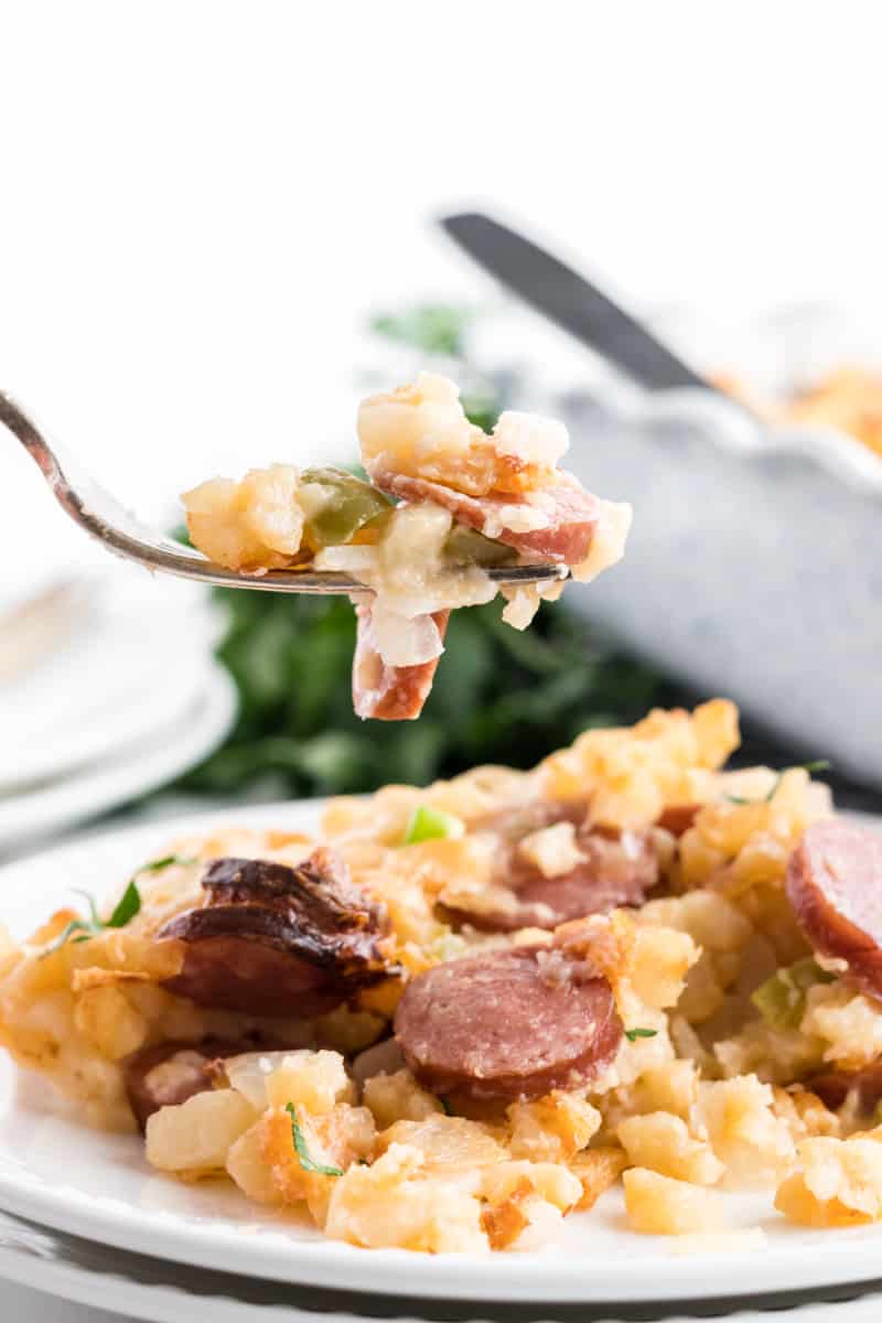 Forkful of smoked sausage cheesy potatoes with plate and casserole dish in background