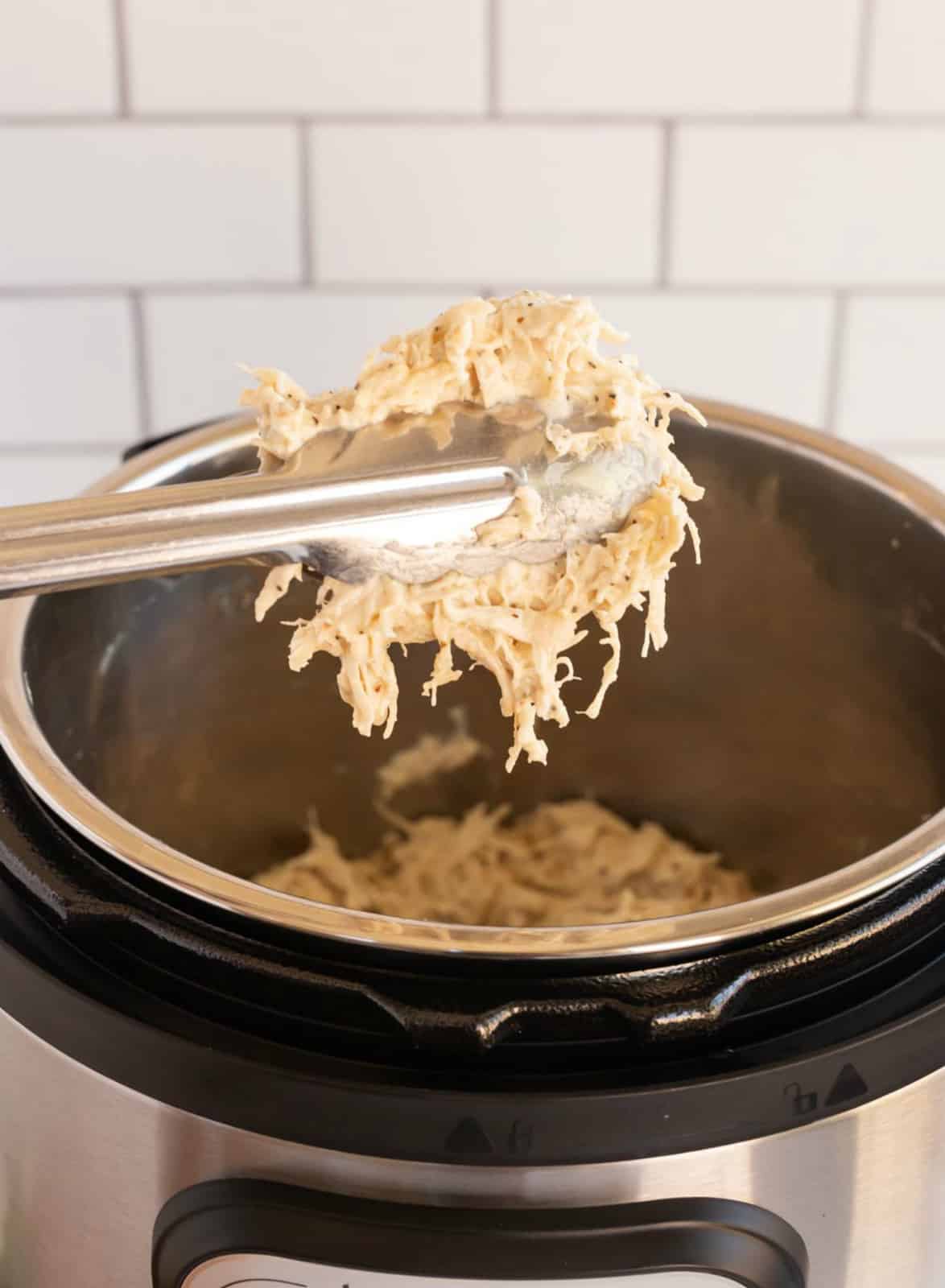 Thongs pulling chicken mixture out of Instant Pot