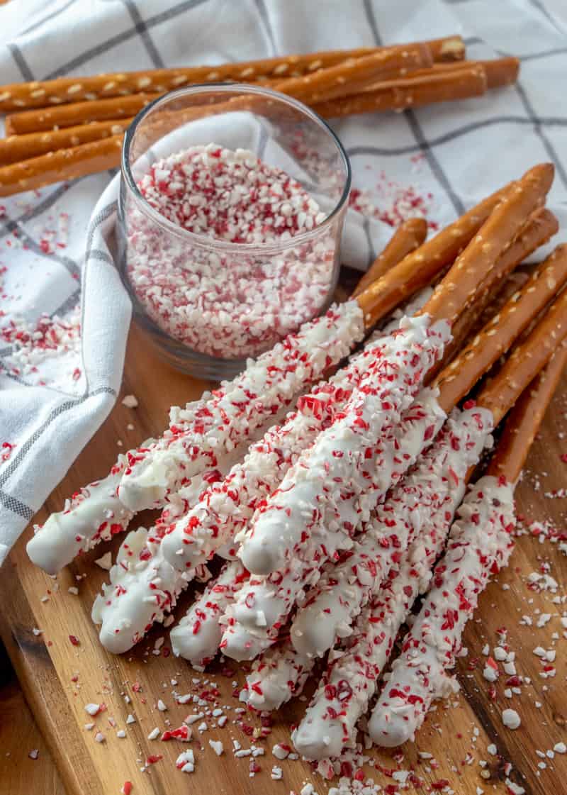 Pretzel Rods stacked on top of one another with cup of crushed candy canes and plane pretzels in background