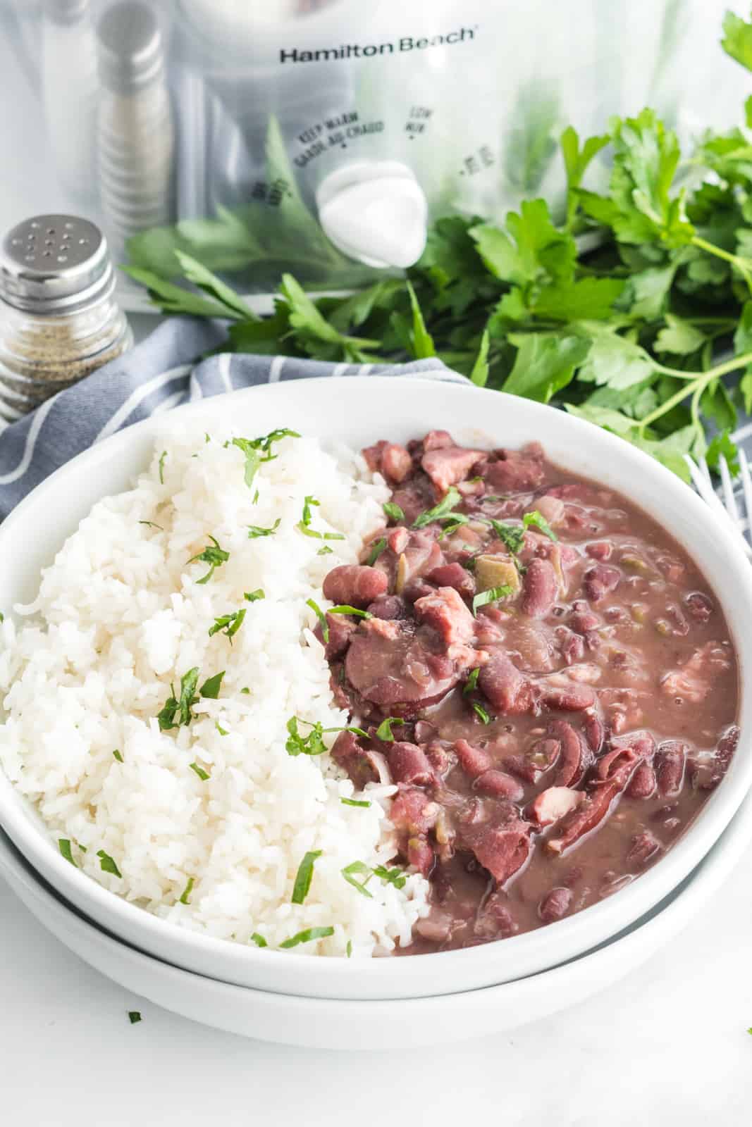 Red beans in rice in bowl with slow cooker and parsley in background