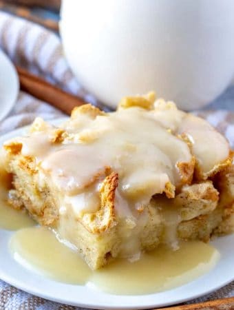 Slice of bread pudding on white plated drizzled with vanilla sauce