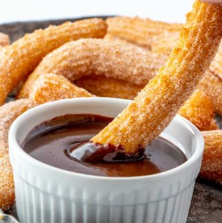 Hand dipping a churro into chocolate sauce