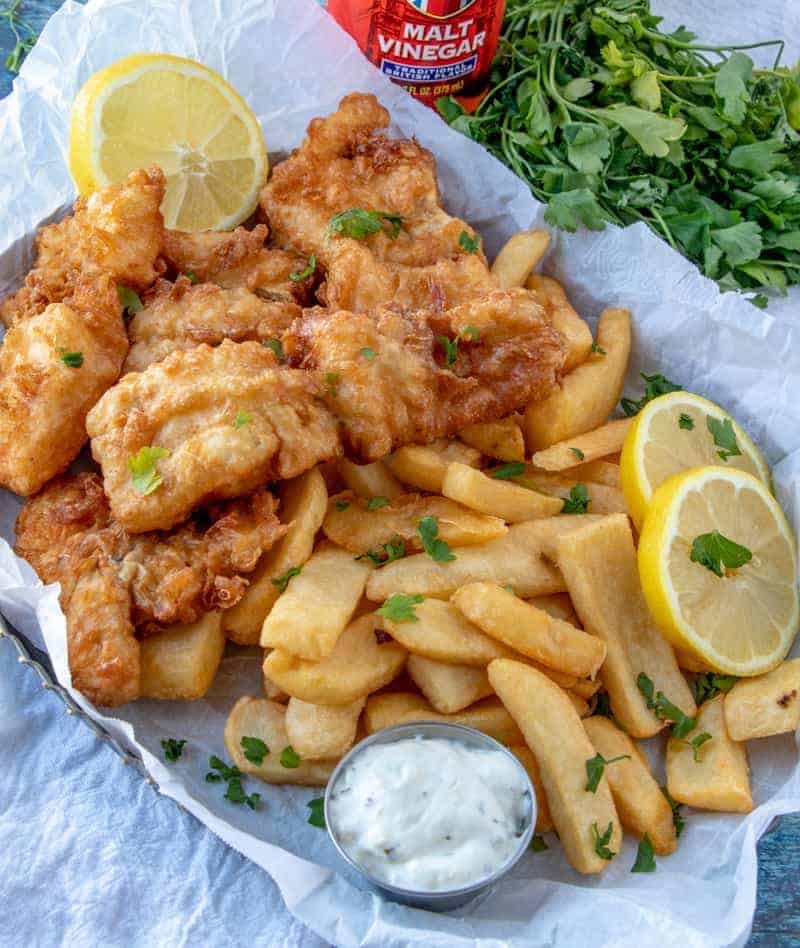 Fish and chips on tray with malt vinegar and parsley in background